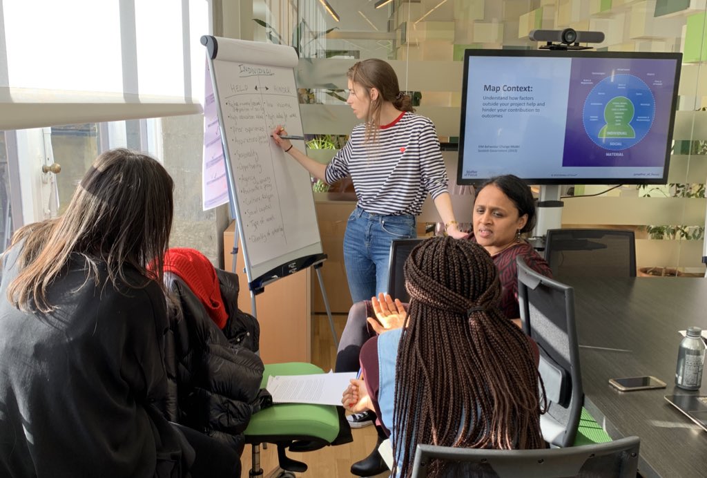 A group of women sit discussing something while a woman writes on a flipchart